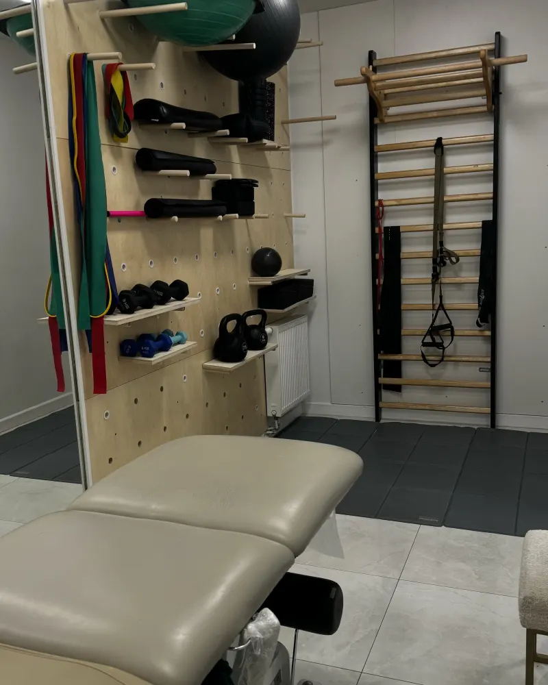 Sala terapii: stół terapeutyczny, ściana ze sprzętem do ćwiczeń i drabinki gimnastyczne